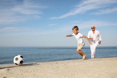 Photo of Cute little boy with grandfather playing football on sea beach