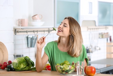 Photo of Woman eating vegetable salad at table in kitchen. Healthy diet