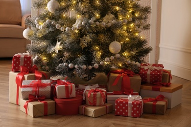 Photo of Pile of gift boxes near beautiful Christmas tree indoors