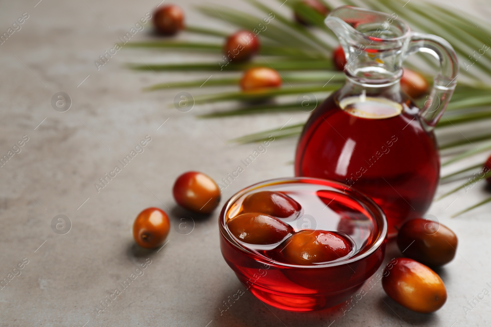 Photo of Palm oil in glass bowl with fruits and tropical leaf on grey table. Space for text