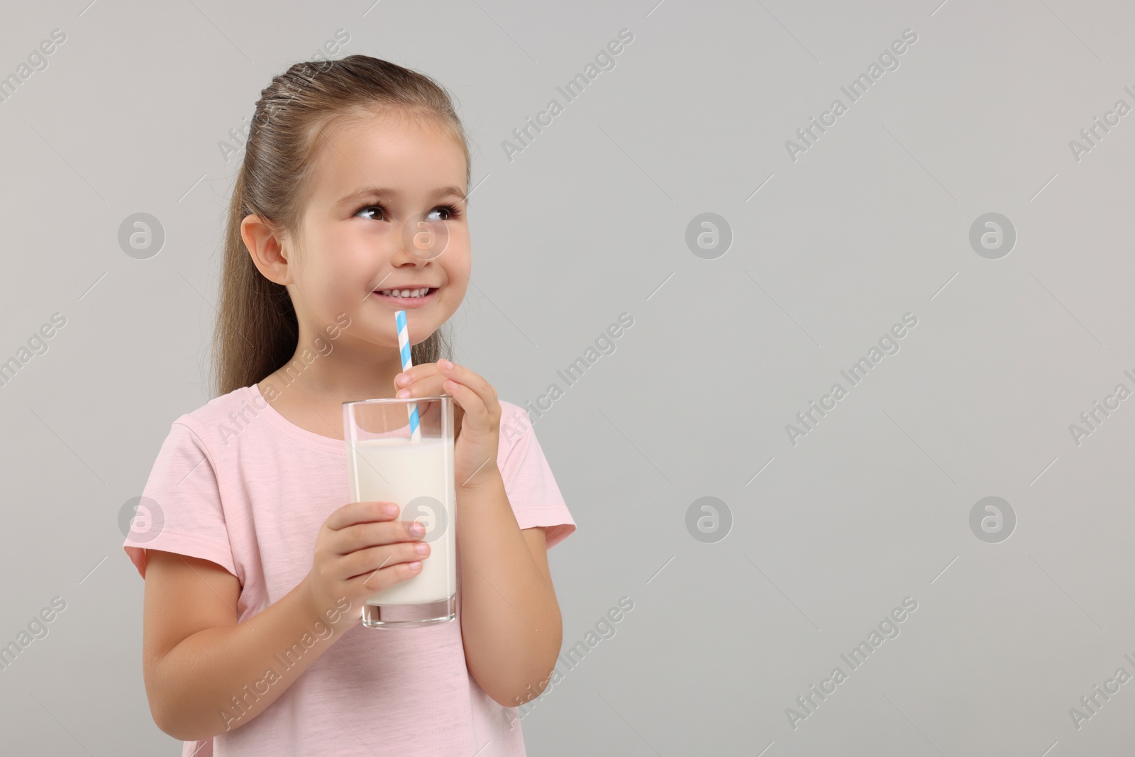 Photo of Cute girl with glass of fresh milk on light grey background, space for text