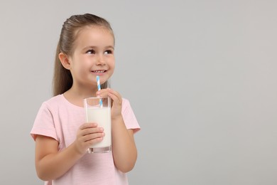 Photo of Cute girl with glass of fresh milk on light grey background, space for text