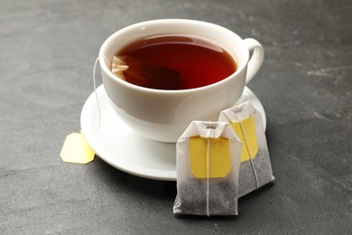 Tea bags and cup of aromatic drink on grey textured table, closeup