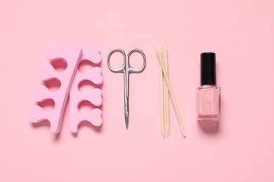 Photo of Nail polish, orange sticks, scissors and toe separators on pink background, flat lay