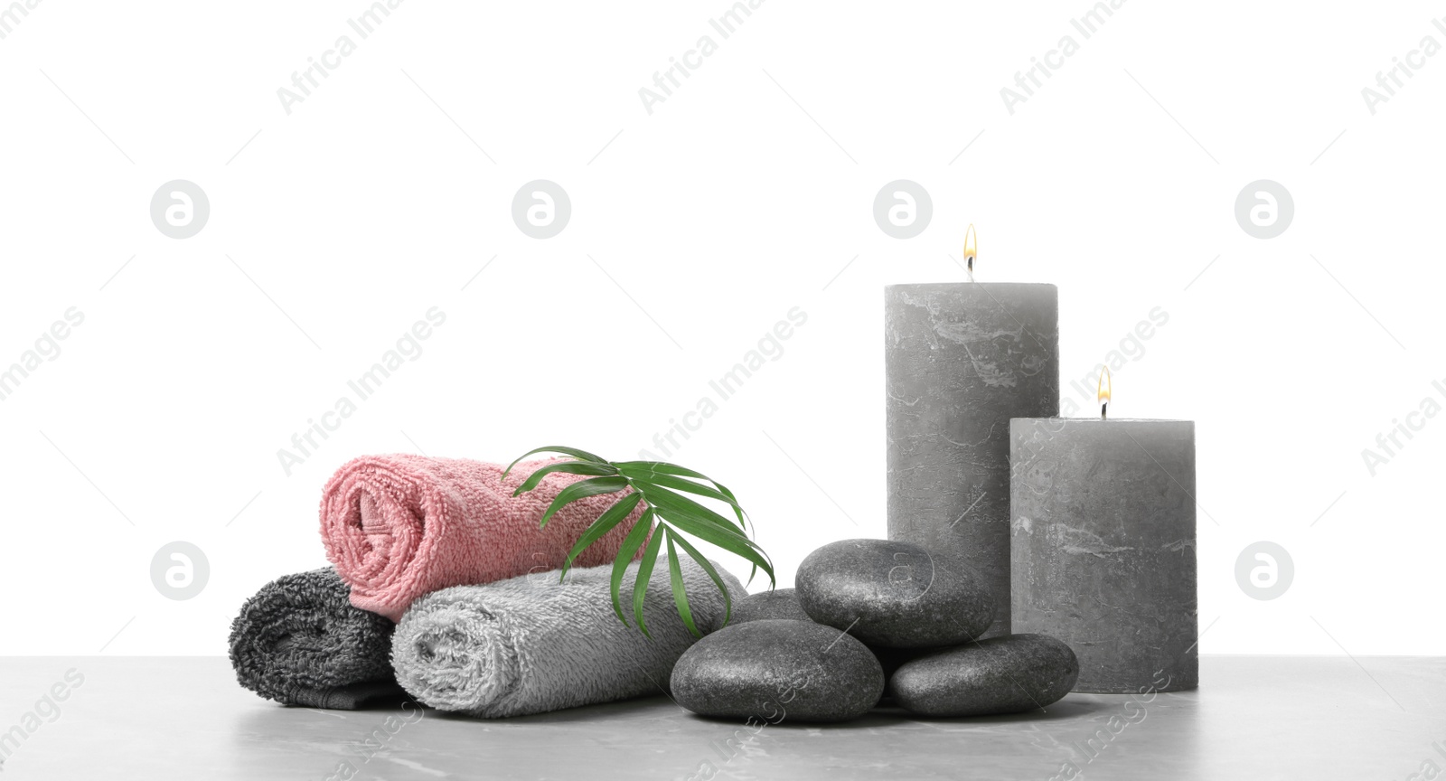 Photo of Spa stones, towels, candles and tropical leaf on light grey table against white background