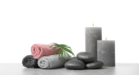 Photo of Spa stones, towels, candles and tropical leaf on light grey table against white background