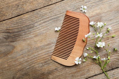 Photo of Comb and small white flowers on wooden background, flat lay. Space for text