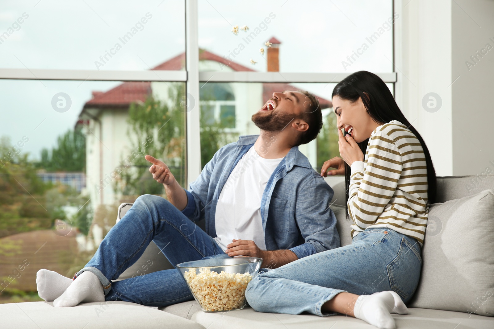 Photo of Happy couple watching movie with popcorn at home