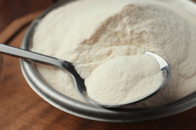 Photo of Bowl and spoon of agar-agar powder on wooden table, closeup