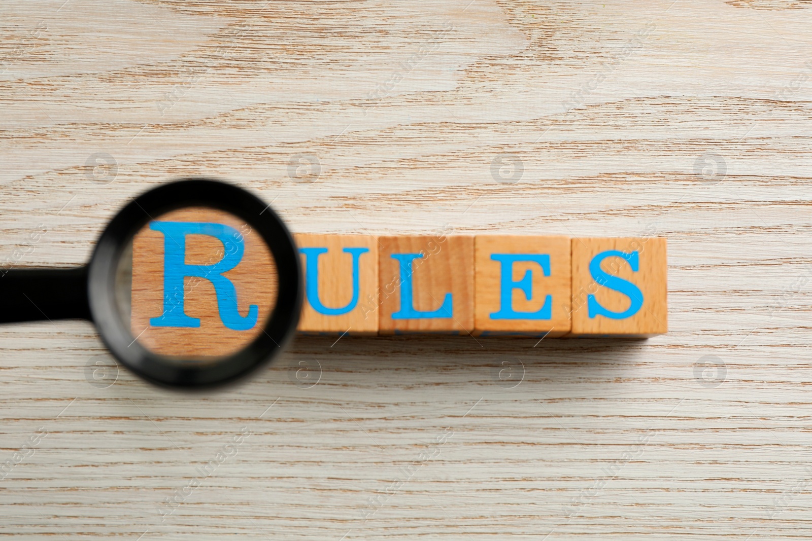 Photo of Magnifying glass over word Rules made of cubes with letters on wooden table, top view