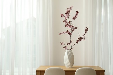 Photo of Blossoming tree twig in vase on wooden table indoors, space for text