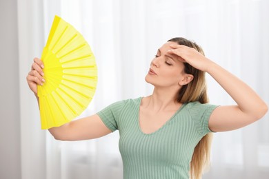 Woman waving yellow hand fan to cool herself at home