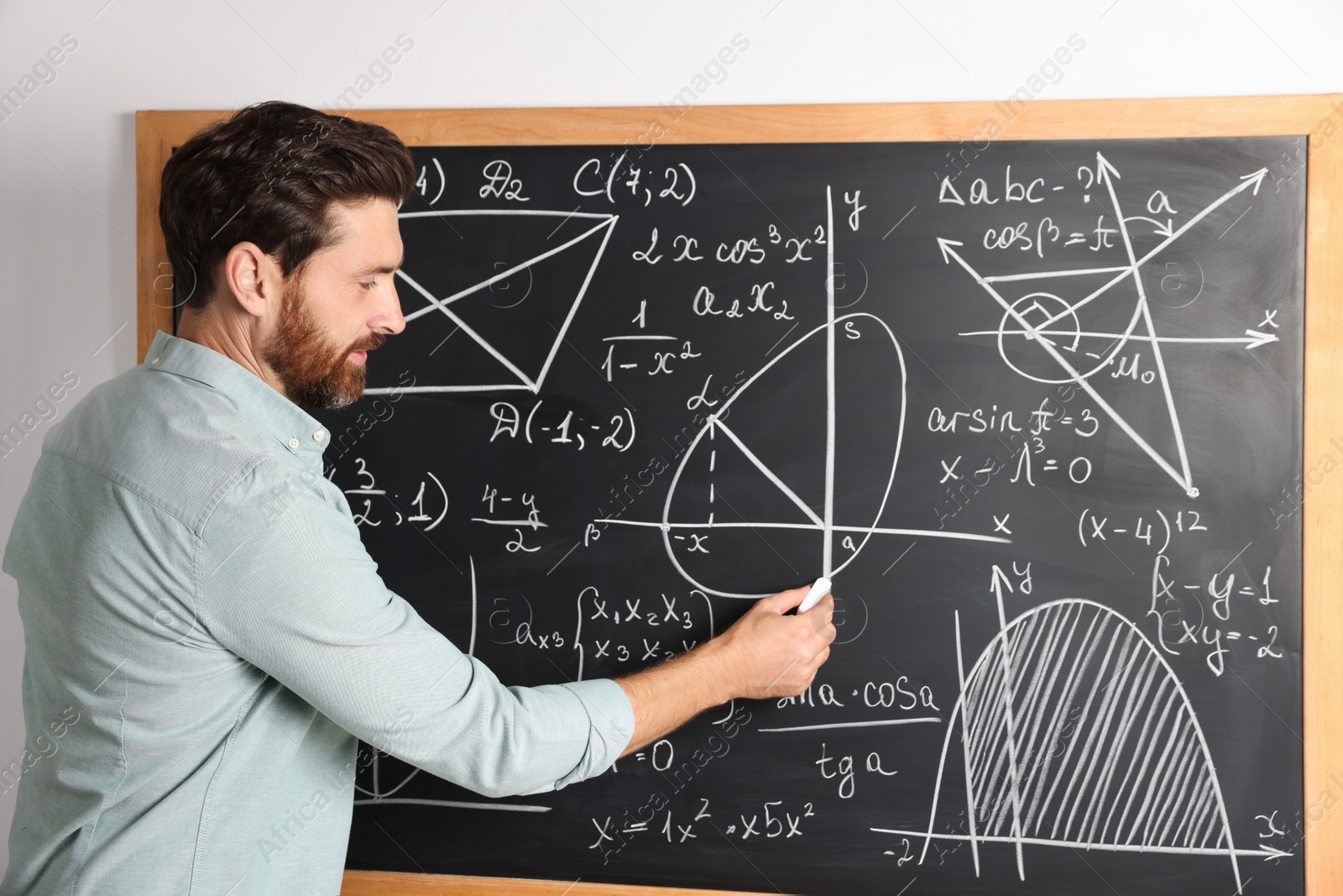 Photo of Mature teacher explaining mathematics at chalkboard in classroom