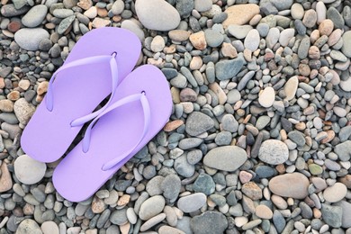 Photo of Stylish violet flip flops on pebble seashore, top view. Space for text