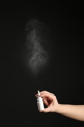 Nasal congestion. Woman spraying remedy from bottle on black background, closeup