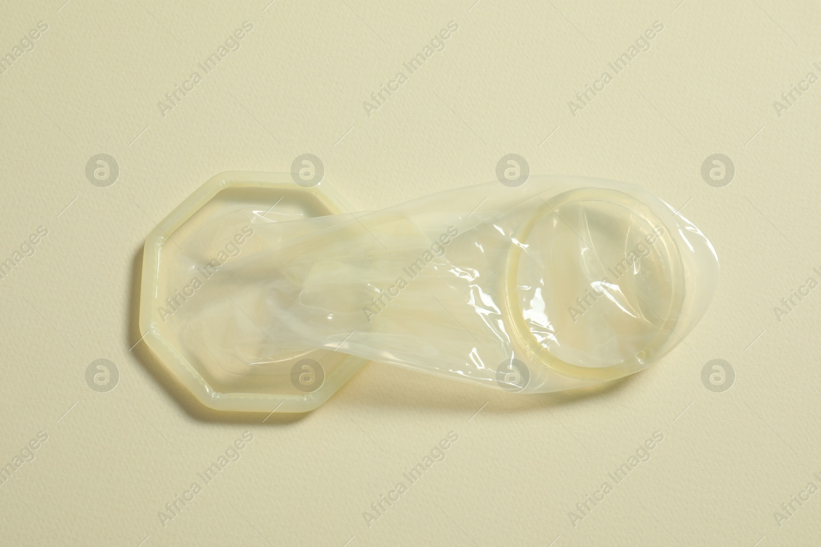 Photo of Unrolled female condom on beige background, top view. Safe sex