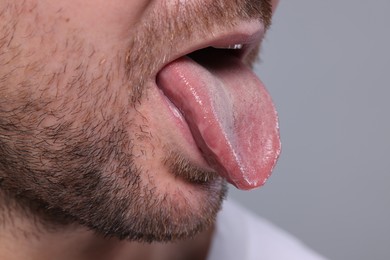 Closeup view of man showing his tongue on grey background, space for text