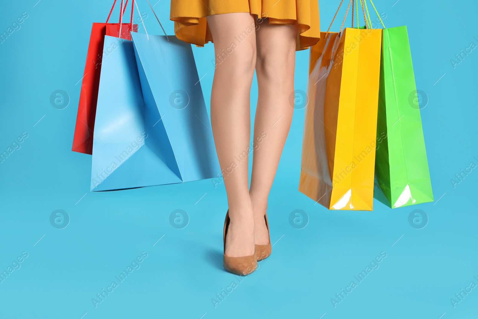 Photo of Woman holding shopping bags on light blue background, closeup. Big sale