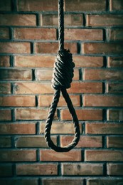 Photo of Rope noose with knot hanging near brick wall