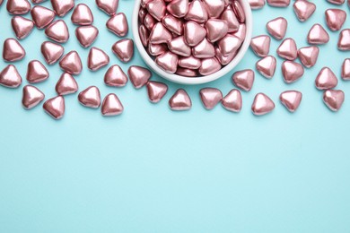 Photo of Bowl and delicious heart shaped candies on light blue background, flat lay. Space for text