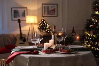 Christmas table setting with burning candles, appetizers and dishware in room