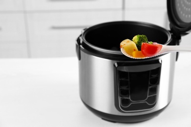Photo of Spoon with vegetables and blurred view of modern multi cooker on background. Space for text