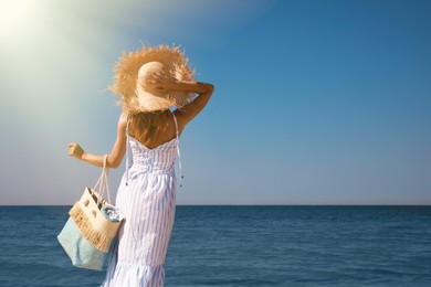 Photo of Woman with beach bag and straw hat near sea, back view. Space for text
