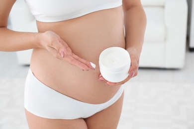 Photo of Pregnant woman holding body cream at home, closeup