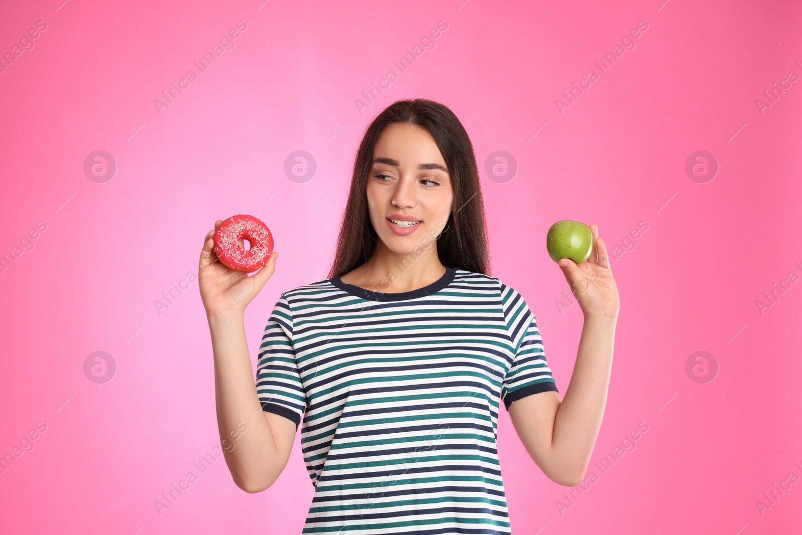 Photo of Woman choosing between apple and doughnut on pink background