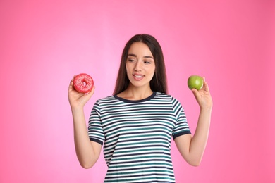 Photo of Woman choosing between apple and doughnut on pink background