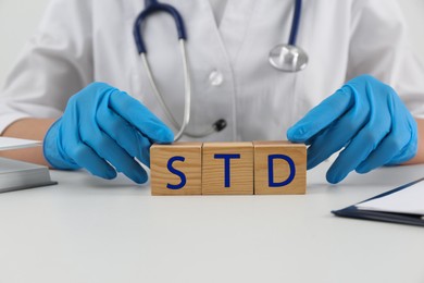 Photo of Doctor and wooden cubes with abbreviation STD at white table, closeup