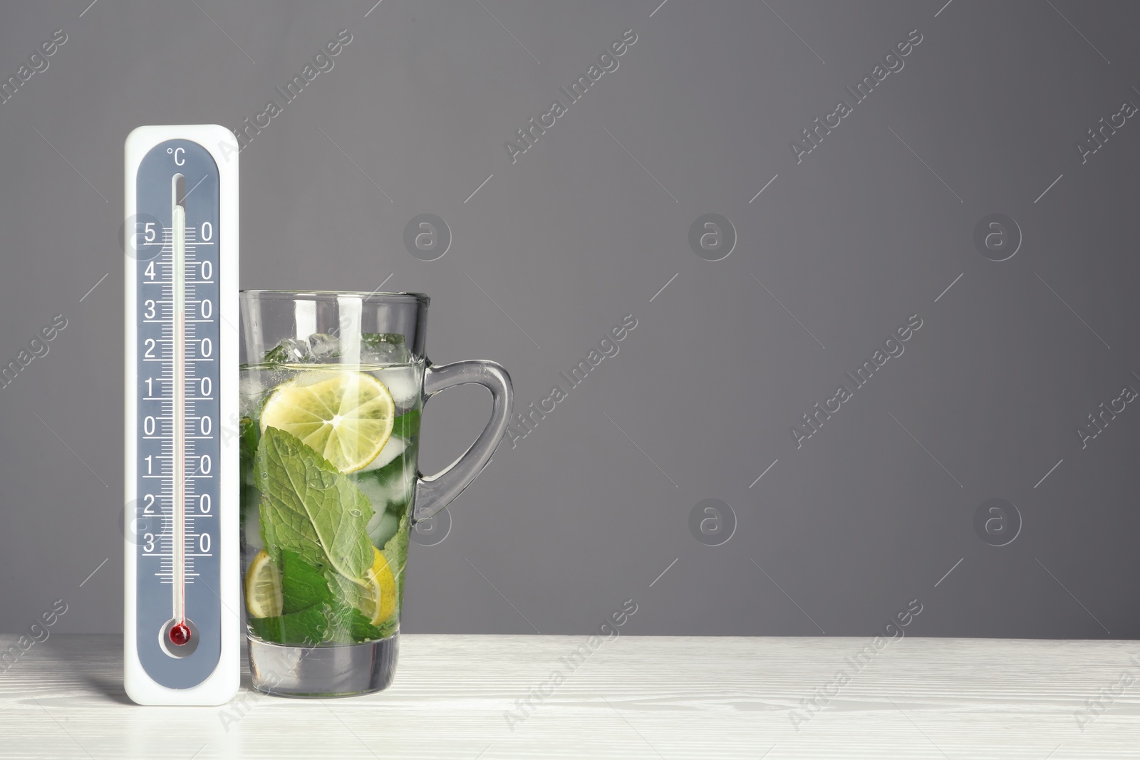 Photo of Thermometer and cup of mojito on wooden table against grey background. Space for text