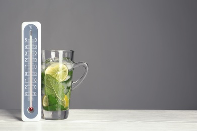 Photo of Thermometer and cup of mojito on wooden table against grey background. Space for text
