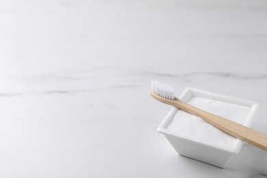 Bamboo toothbrush and bowl of baking soda on white table, closeup. Space for text