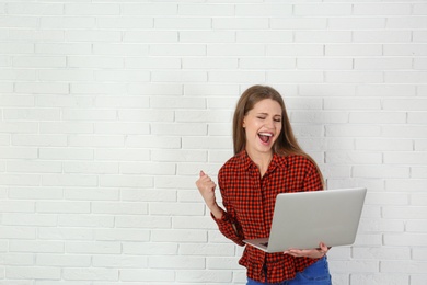 Photo of Emotional young woman with laptop celebrating victory near brick wall. Space for text