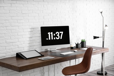 Photo of Modern workplace interior with computer and devices on table near brick wall