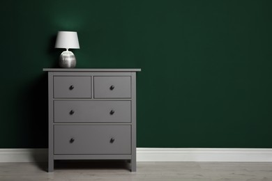 Photo of Modern chest of drawers with lamp near green wall indoors. Space for text
