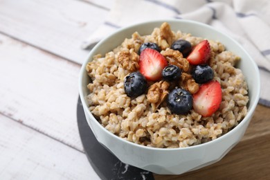 Photo of Tasty oatmeal with strawberries, blueberries and walnuts in bowl on white wooden table. Space for text