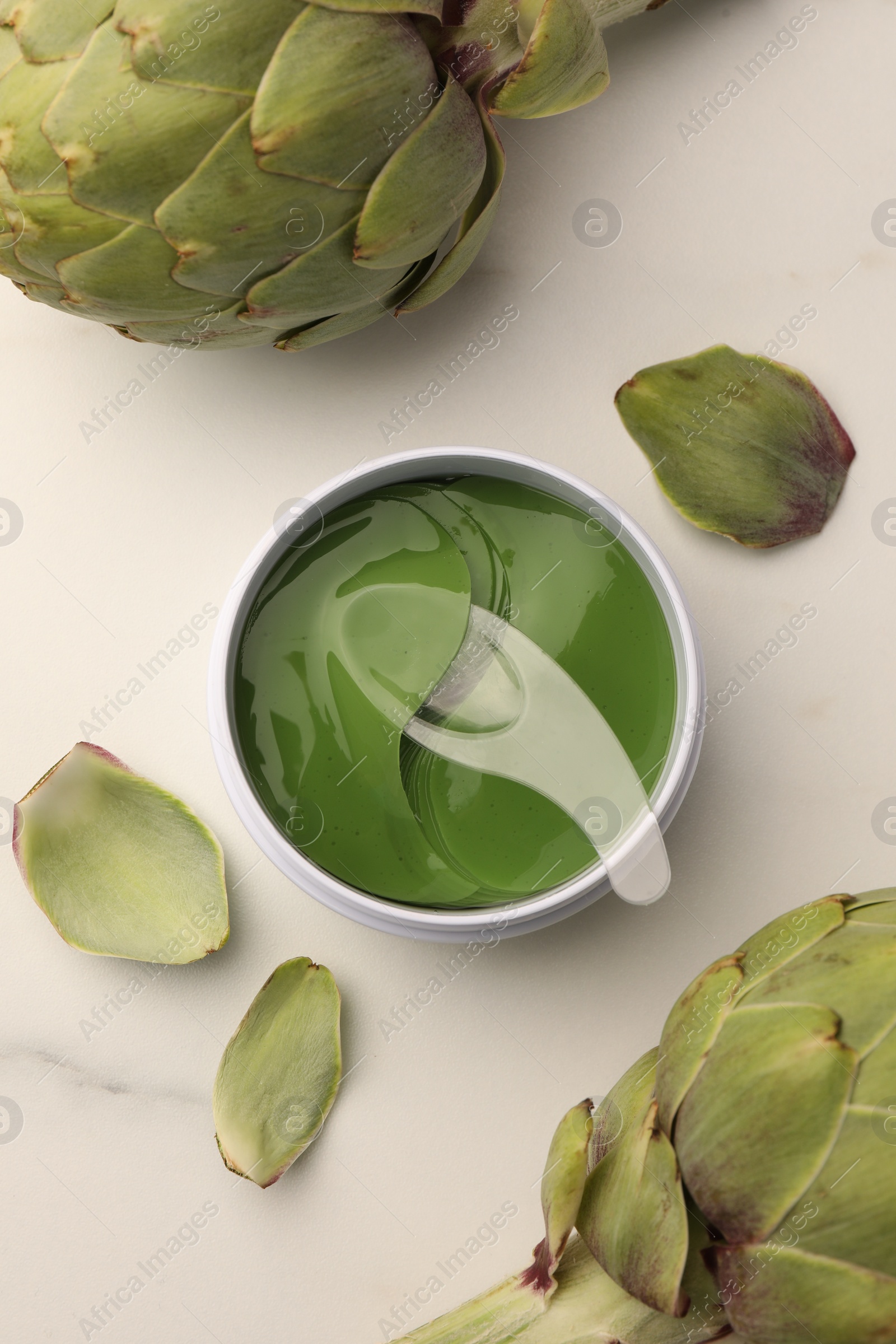 Photo of Package of under eye patches and artichokes on white marble table, flat lay. Cosmetic product