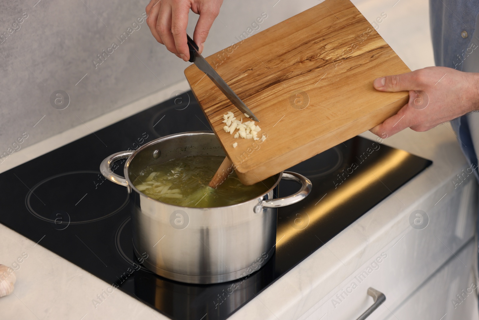 Photo of Man adding garlic into soup in kitchen, closeup