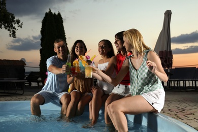 Photo of Happy people with refreshing drinks enjoying fun pool party in evening