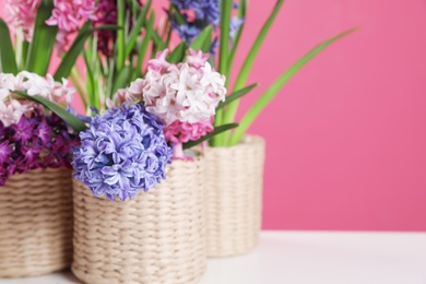 Photo of Beautiful hyacinths in wicker pots on table against color background, space for text. Spring flowers