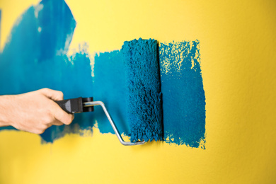 Photo of Man painting yellow wall with blue dye, closeup