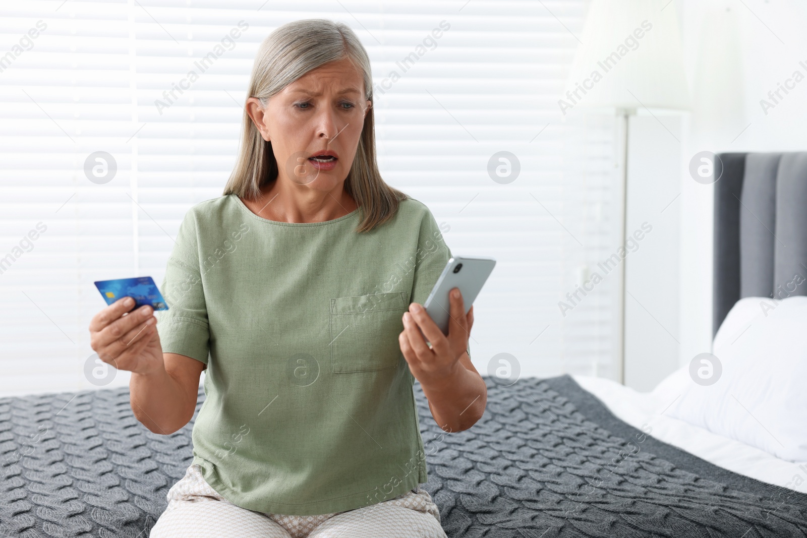 Photo of Worried woman with credit card and smartphone in bedroom, space for text. Be careful - fraud