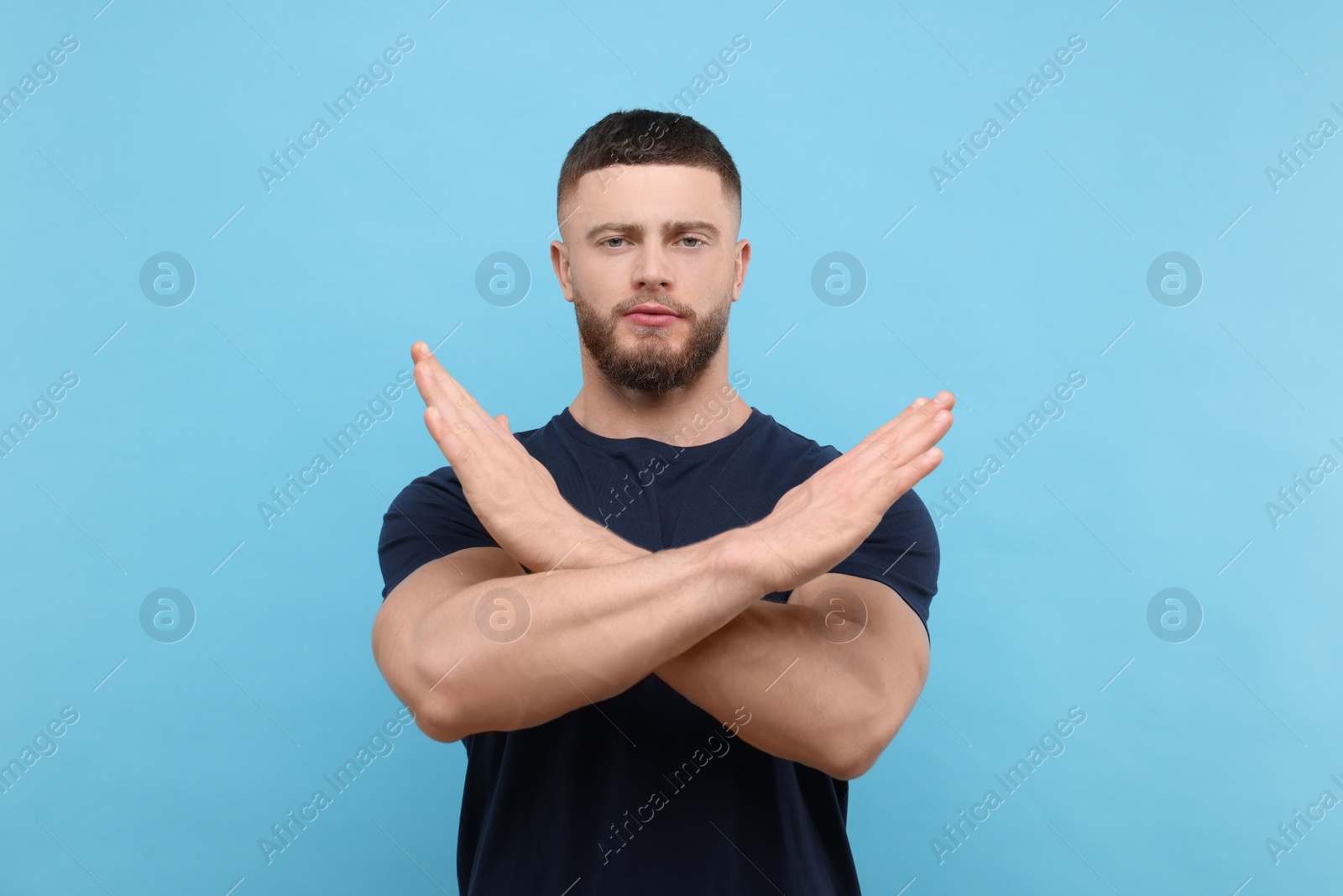 Photo of Stop gesture. Man with crossed hands on light blue background