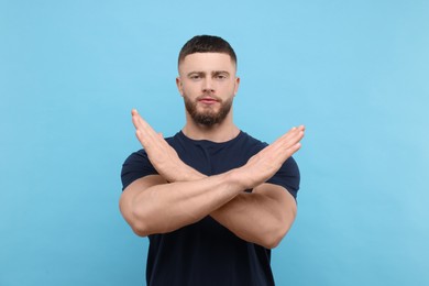 Photo of Stop gesture. Man with crossed hands on light blue background
