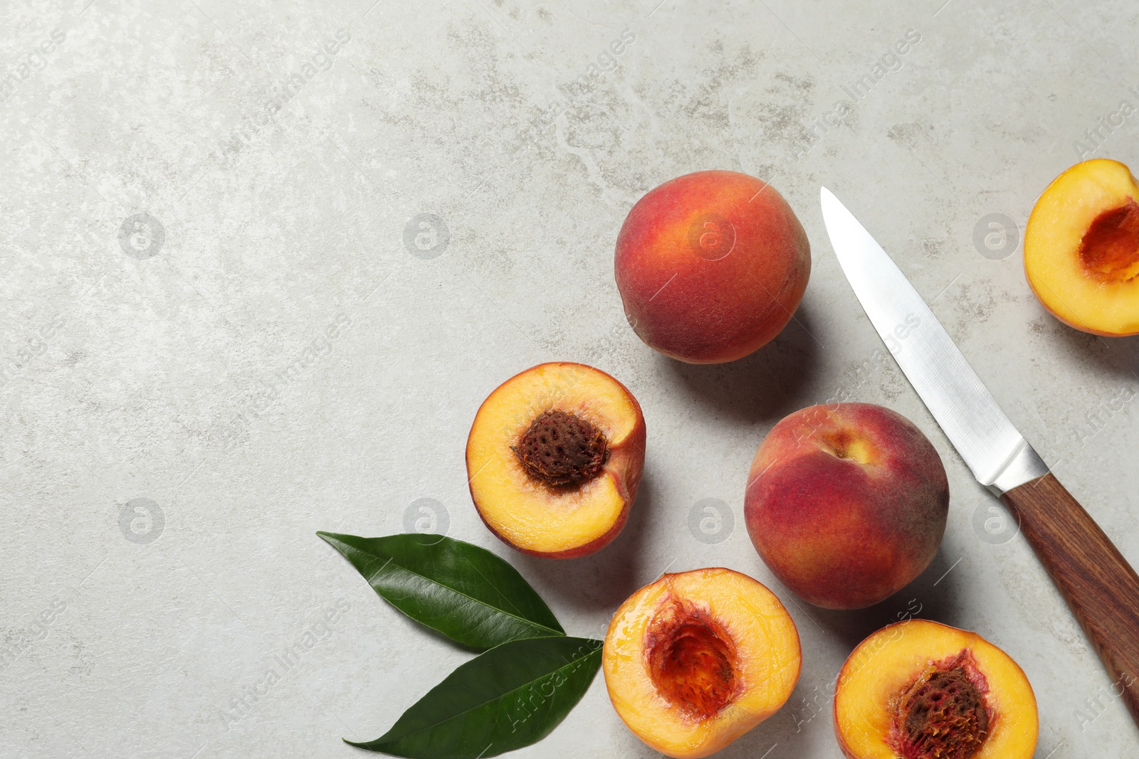 Photo of Delicious juicy ripe peaches, leaves and knife on light grey textured table, flat lay. Space for text