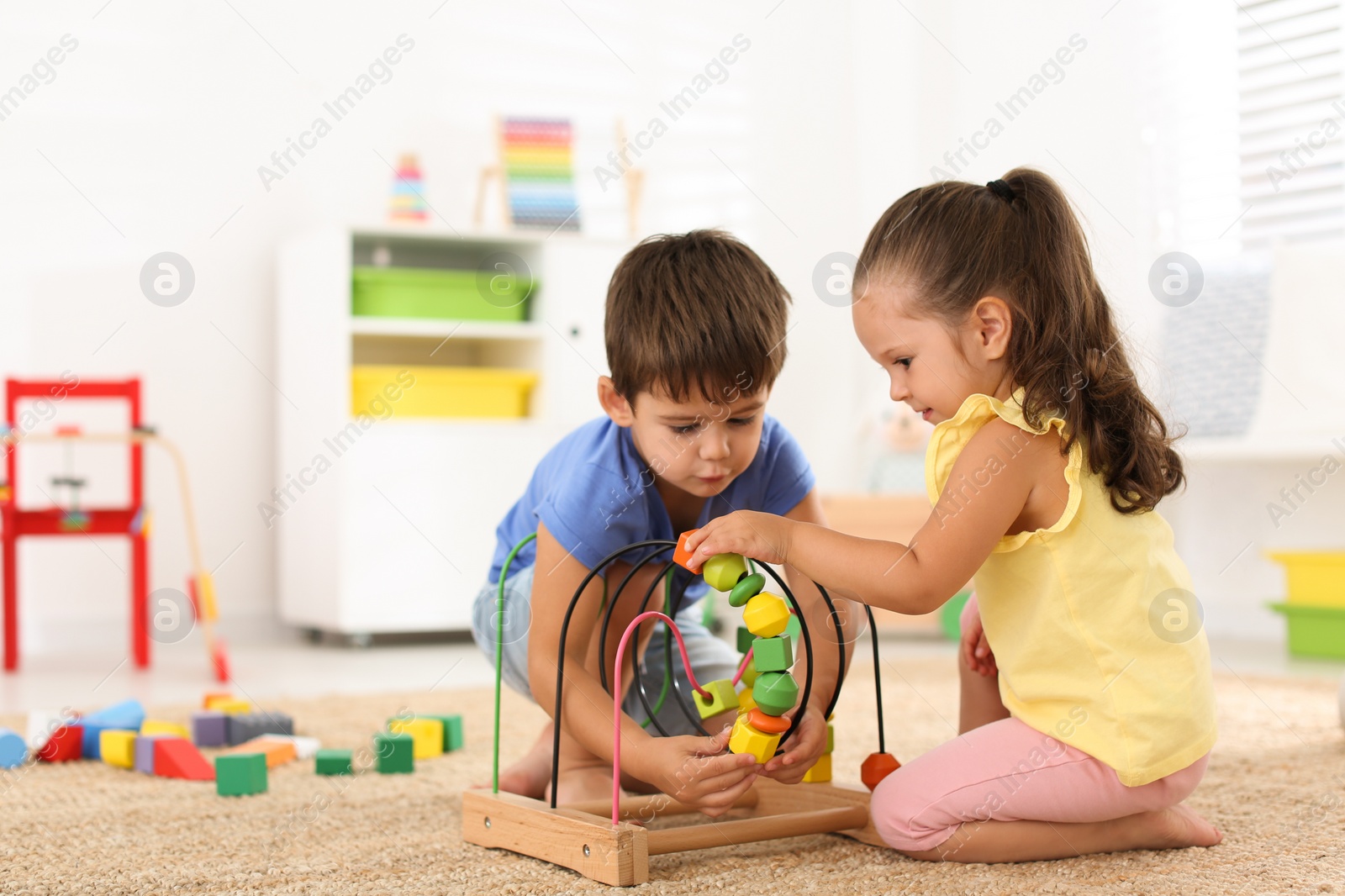 Photo of Cute little children playing with bead maze on floor at home. Educational toy