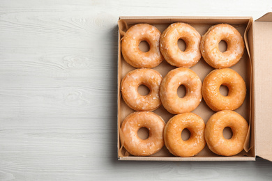 Photo of Delicious donuts on white wooden table, top view. Space for text