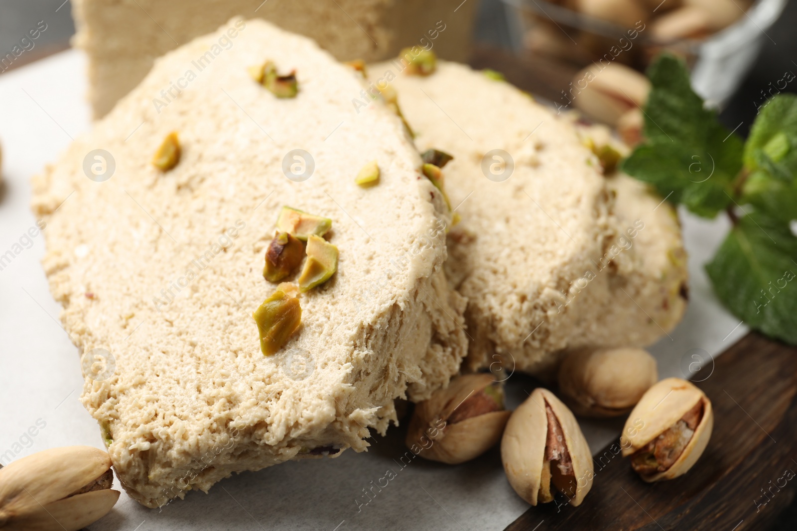 Photo of Tasty halva with pistachios and mint on table, closeup